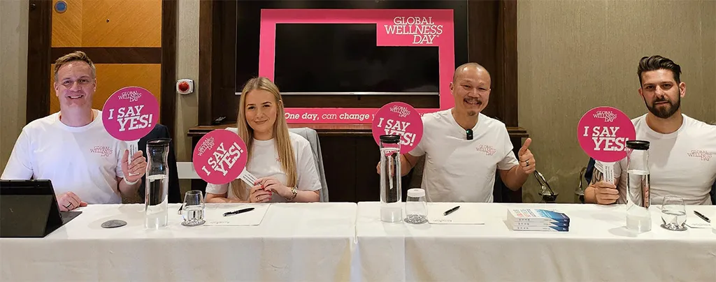Frven speaking at Jumeirah Global Wellness Day panel - four panelists at discussion table with 'I Say Yes!' signs and Global Wellness Day branding