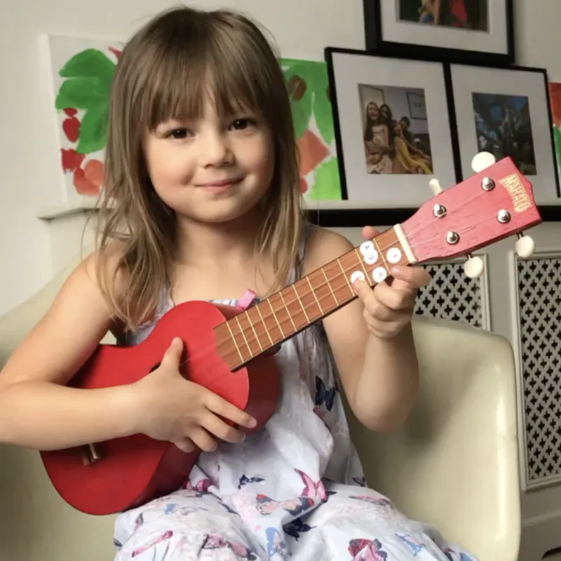 Young girl playing red ukulele, smiling